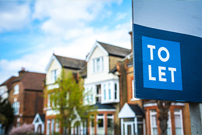 To let sign in front of residential properties with lush greenery and blue sky background highlighting rental options in the area perfect for two tenants.