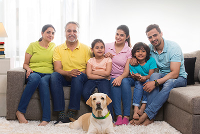 A happy family of six sits together on a couch with a friendly dog in front of them in a bright living room showcasing love and togetherness for generations including children and grandparents celebrating special moments.